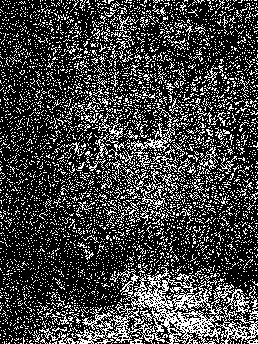 A very pixelated black and white image of a bedroom, posters and collages on the wall, the douvet on the bed is messy, a stuffed toy, bowl with spoon, and notebook lie on the unmade bed