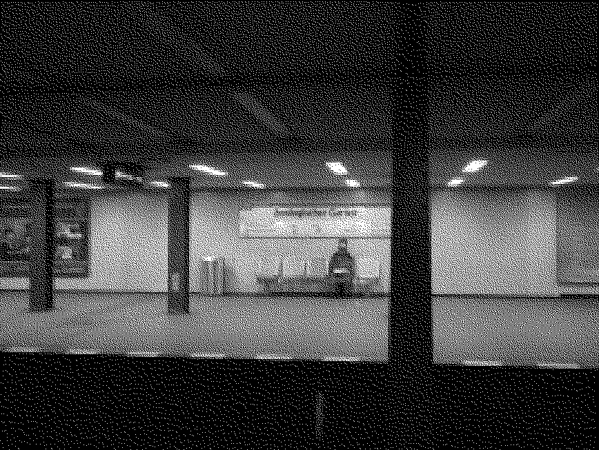 Black and white image of a metro station, a lady sits alone on a bench on the other side of the platform